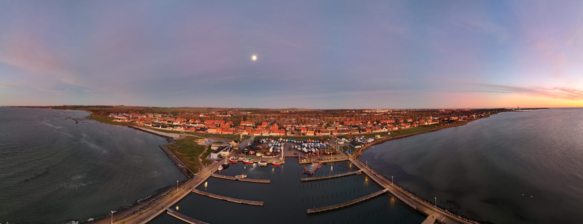 Panorama över marinan och stan i skymning med månen